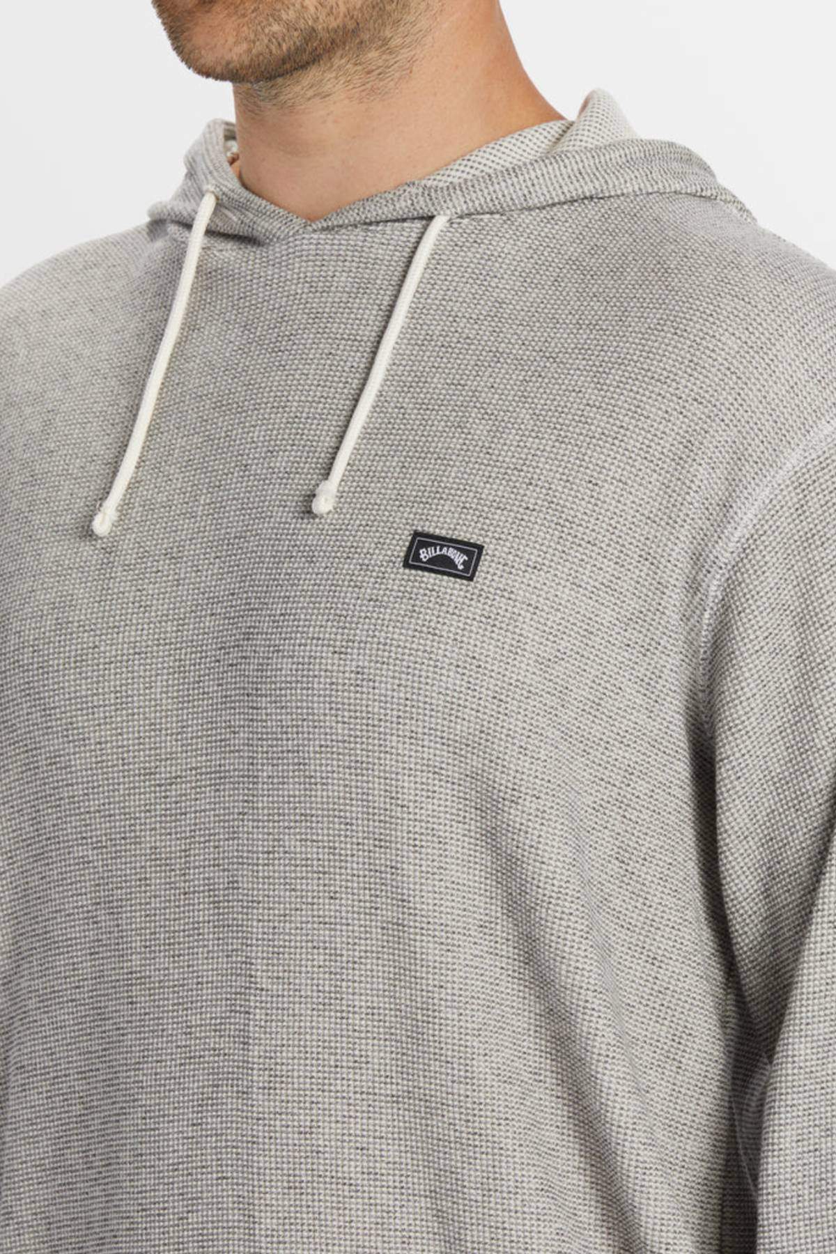 A person wears the Billabong Keystone Pullover, a light gray waffle knit thermal hoodie with white drawstrings and a small black chest logo. The image is cropped to show only the lower face, shoulders, and upper chest.