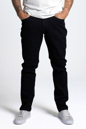 Wearing the BLKWD Vassnik Denim Jean Slim Fit, a person stands with hands in pockets against a plain light background. Only their legs and lower torso are visible, styled with white sneakers and a white t-shirt.