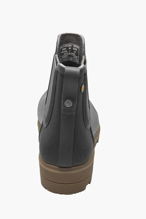 A close-up rear view of the BOGS Holly Chelsea Waterproof Boot in dark gray shows its brown sole, ribbed back texture, small round logo near the heel, and BLOOM Algae Footbeds for comfort.
