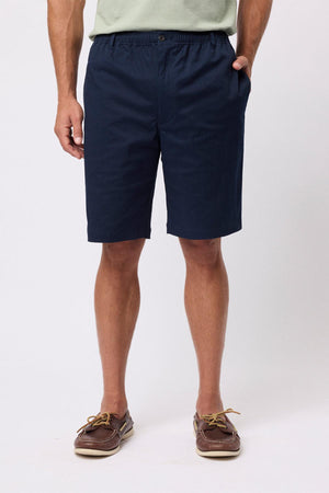 A person wearing navy blue Breakaway Cody Shorts with an elastic waistband, a light green shirt, and brown boat shoes stands hands in pockets against a plain white background—perfect for everyday style.