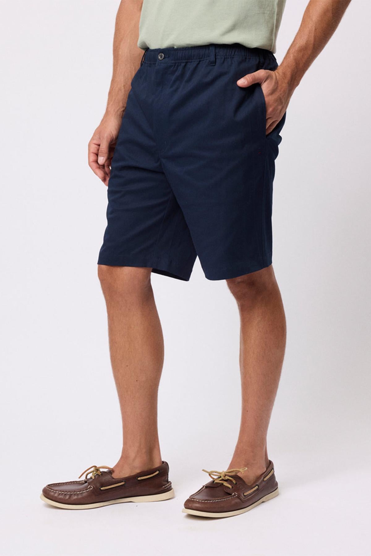 A person stands against a plain white background with hands in pockets, wearing a light green T-shirt, Breakaway Cody Shorts with an elastic waistband, and brown boat shoes—ideal for effortless everyday style.