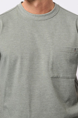 A person wears the Breakaway Kinnersly Crew, a light gray-green crew neck t-shirt featuring a left chest pocket, shown from shoulders to mid-torso. The lightweight fabric provides comfort and a relaxed fit.