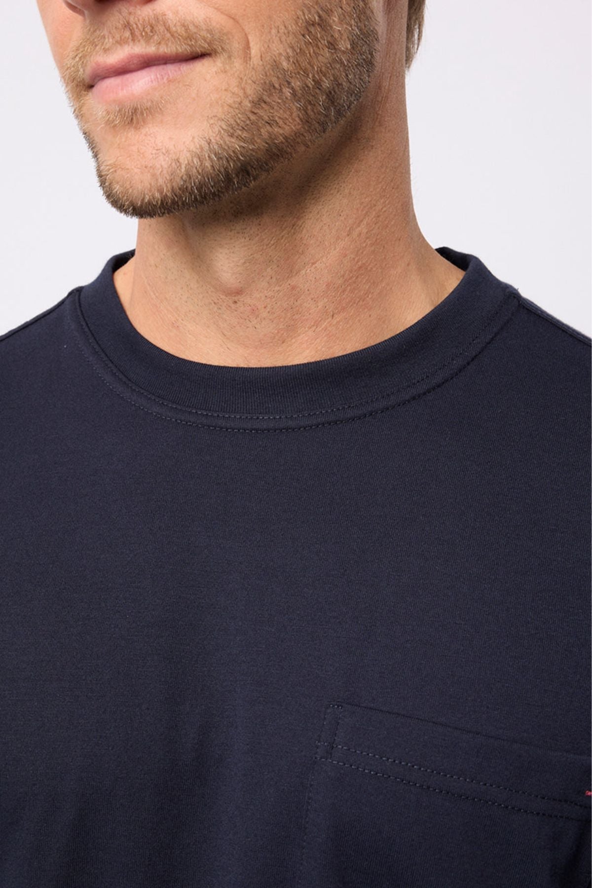 A close-up of a man in the Breakaway Kinnersly Crew, a dark navy crewneck t-shirt with a left chest pocket. The relaxed fit tee shows only his lower face, neck, and upper chest.