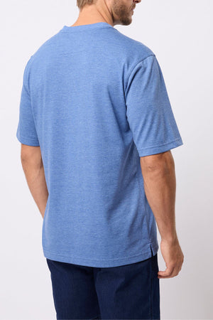 A man stands with his back to the camera, wearing the Breakaway Kinnersly Crew, a relaxed fit blue short-sleeve t-shirt, paired with lightweight dark blue shorts against a plain white background.
