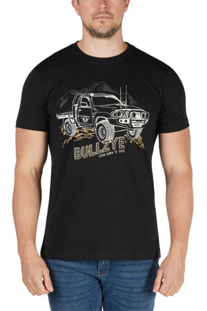 A man wears the Bullzye Dusk Tee, featuring an illustrated off-road truck, mountains, and "FROM DAWN TO DUSK" on the front. Made from soft cotton jersey, this classic tee pairs perfectly with his blue jeans.