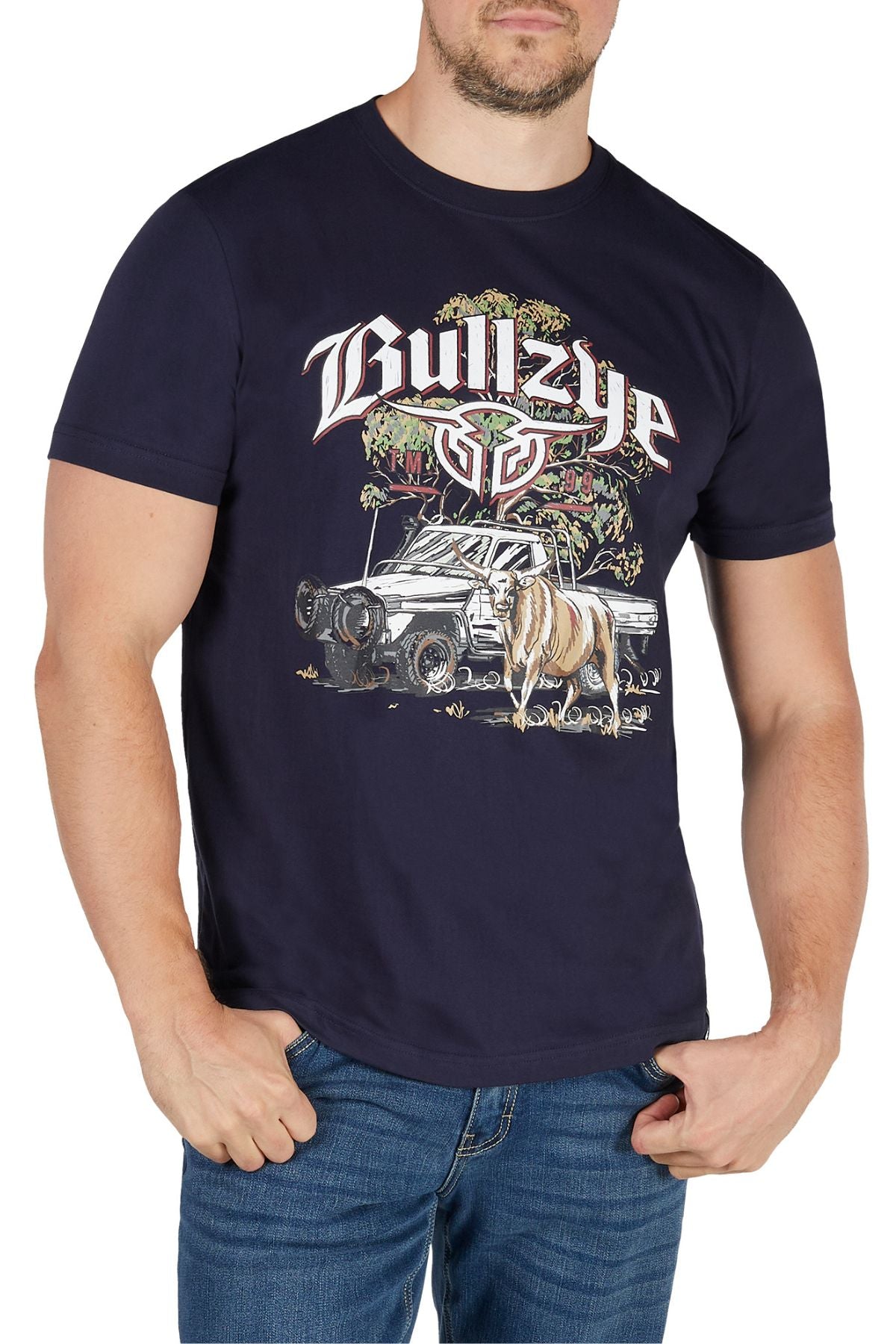 A man stands with his hands in his jeans pockets, wearing the Bullzye Dusk Tee— a classic navy blue 100% cotton jersey t-shirt featuring "Bullzye" text, a bull graphic, and an off-road vehicle.