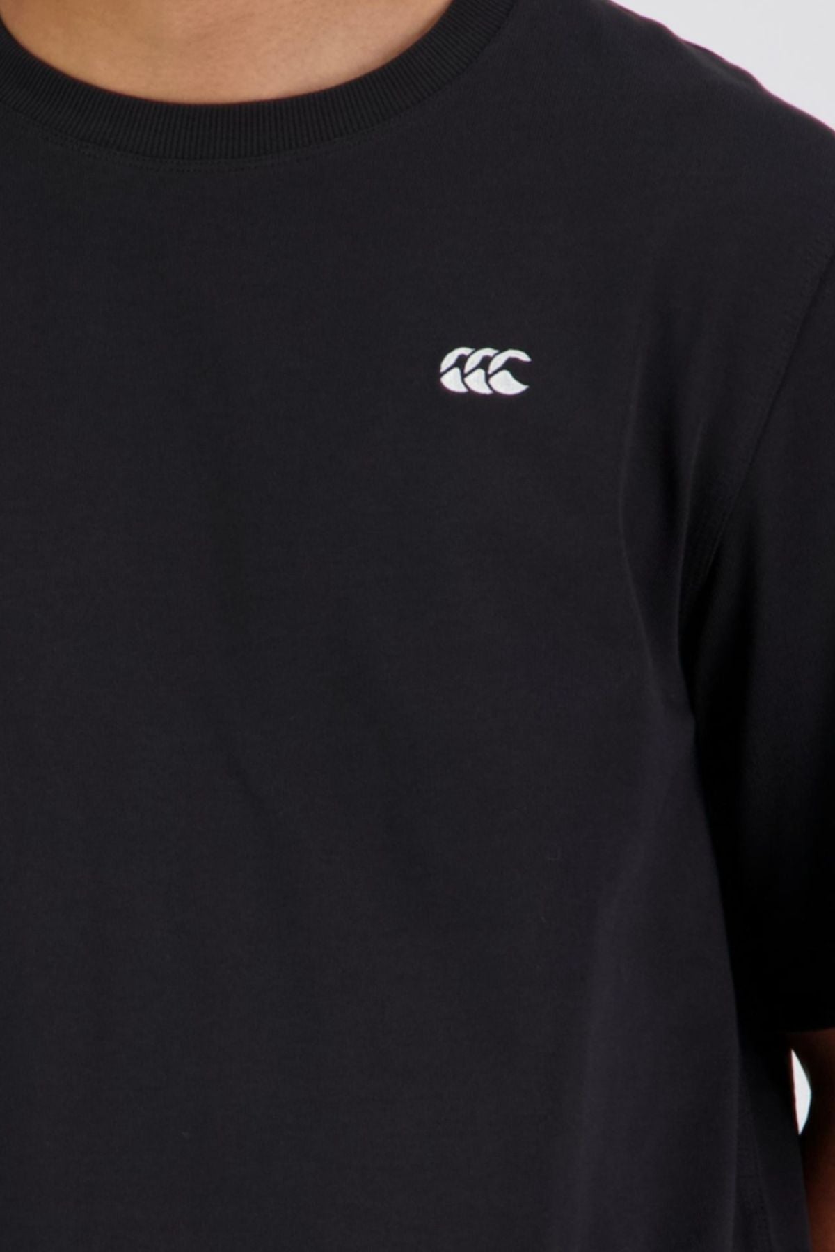 A person wearing the Canterbury CCC Collection T-Shirt, a plain black tee with a small white logo on the left chest, featuring an oversized fit and made from 100% cotton for comfort.