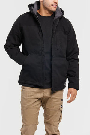 A person wearing the CAT Hooded Sherpa Lined Jacket over a black shirt and tan cargo pants stands with one hand in their pocket against a plain, light background.