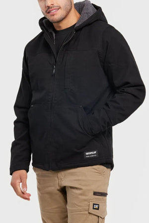 A person wearing a black CAT Hooded Sherpa Lined Jacket with a gray lining and tan work pants with pockets and a “CAT” logo patch, standing against a plain light background.