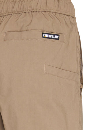 Close-up of the back pocket area on CAT Hydraulic Short, tan stretch work shorts with an elastic waistband, Caterpillar label above the pocket, and visible stitching.