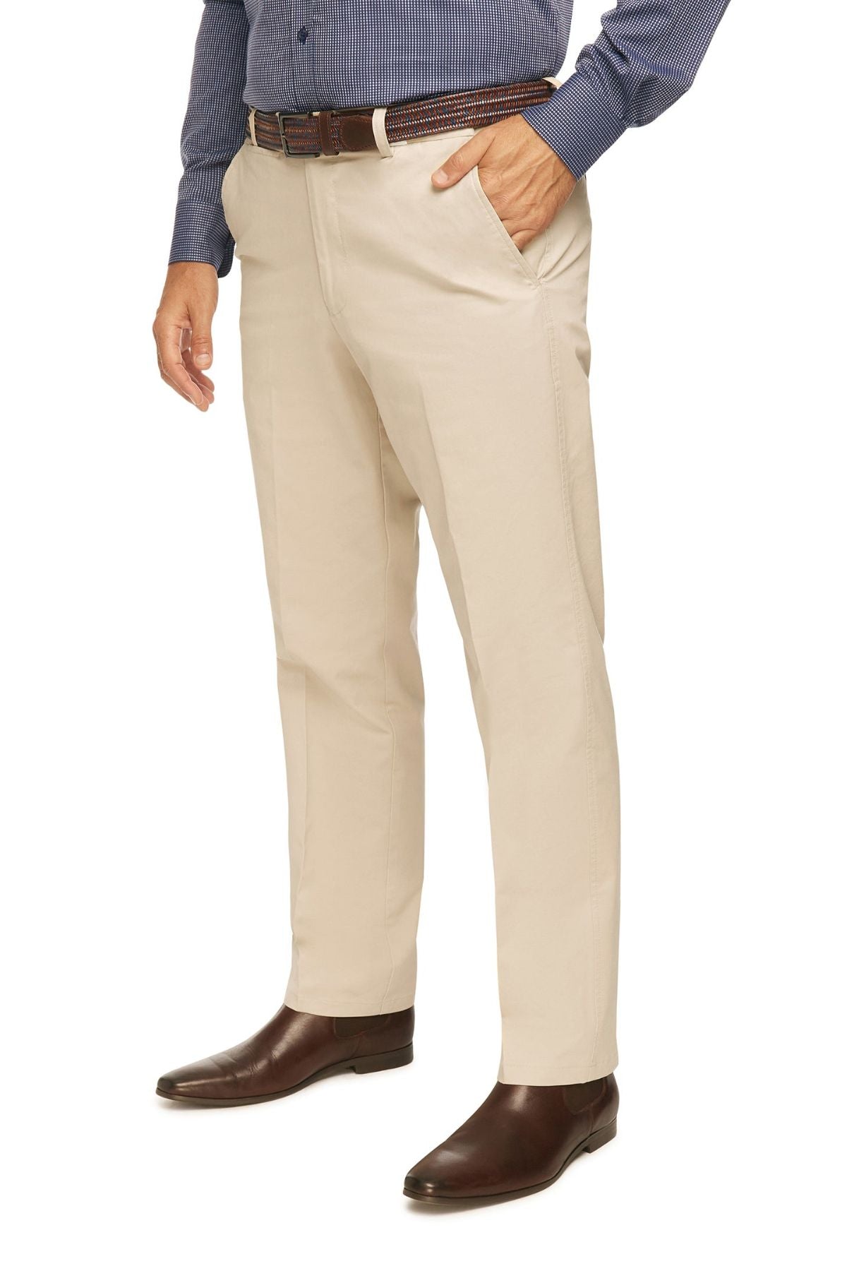 A person wearing beige City Club Mariner Harbour Pants with elasticated sides, a dark blue long-sleeve button-down shirt, and brown leather dress shoes. The person has one hand in their pocket. The photo is cropped to show only from the shoulders down to the feet against a white background.