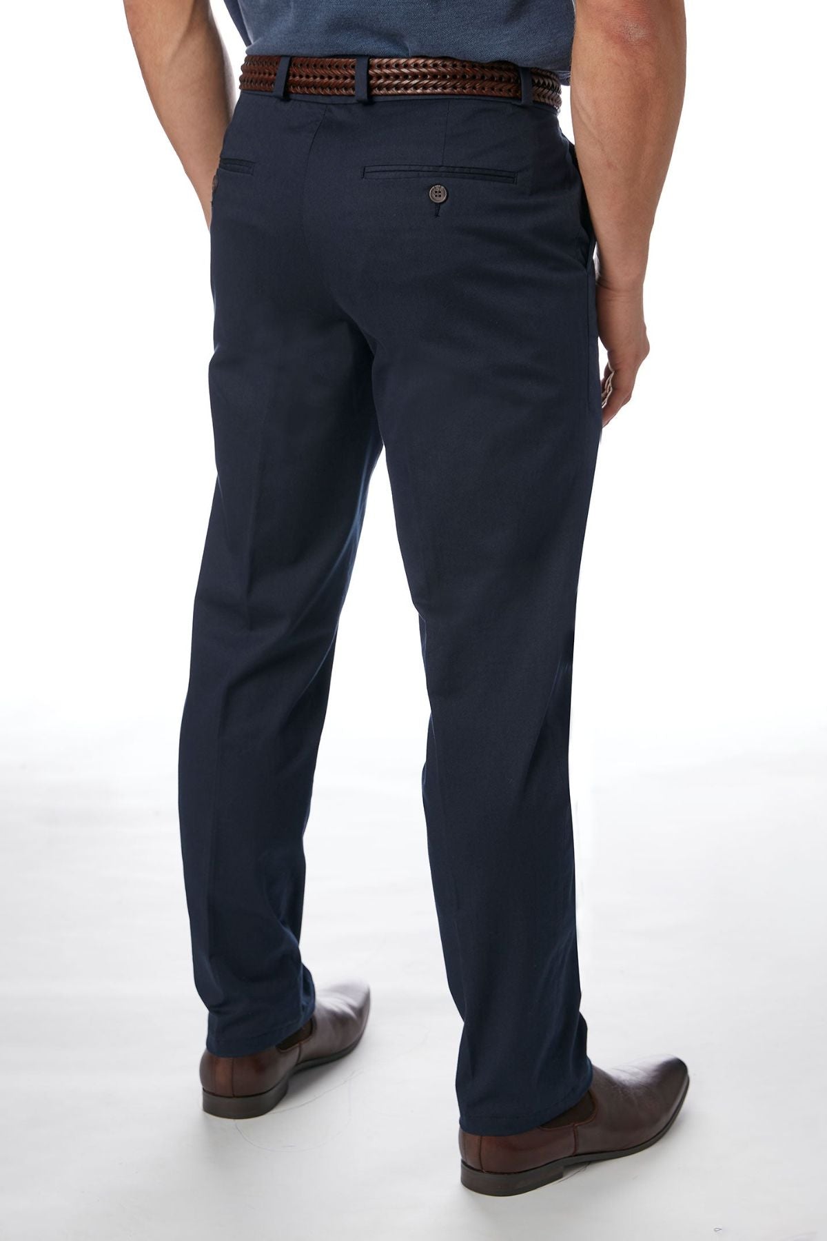 A person is standing with their back to the camera, showcasing the stylish and comfortable City Club Navigator 1770 Pants. They are wearing dark blue, slim-fit trousers paired with a woven brown belt and brown shoes. Made from Cotton and Spandex, these trousers fit perfectly. The plain white background ensures that the person remains the main focus of the image.
