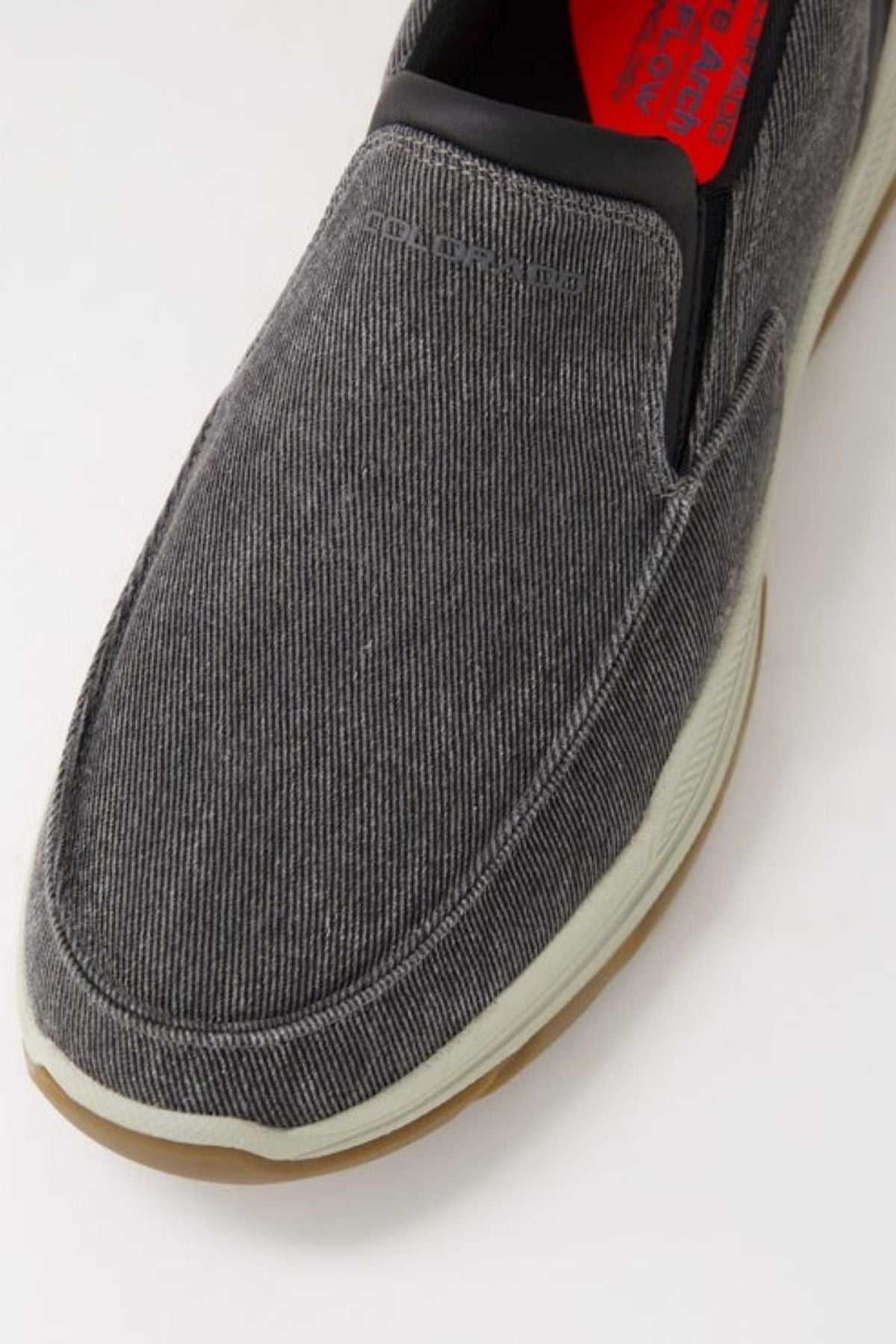 Close-up of the Colorado Kanza Canvas Shoe: gray slip-on with textured fabric upper, white midsole, brown slip-resistant outsole, visible elastic panel, and red insole with printed text.