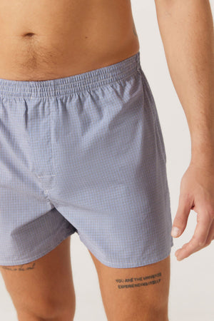Wearing Contare Cotton 2 Pack Check Boxer Shorts with an elastic waist, a person stands against a plain background, showing the lower torso and tattooed upper thighs.