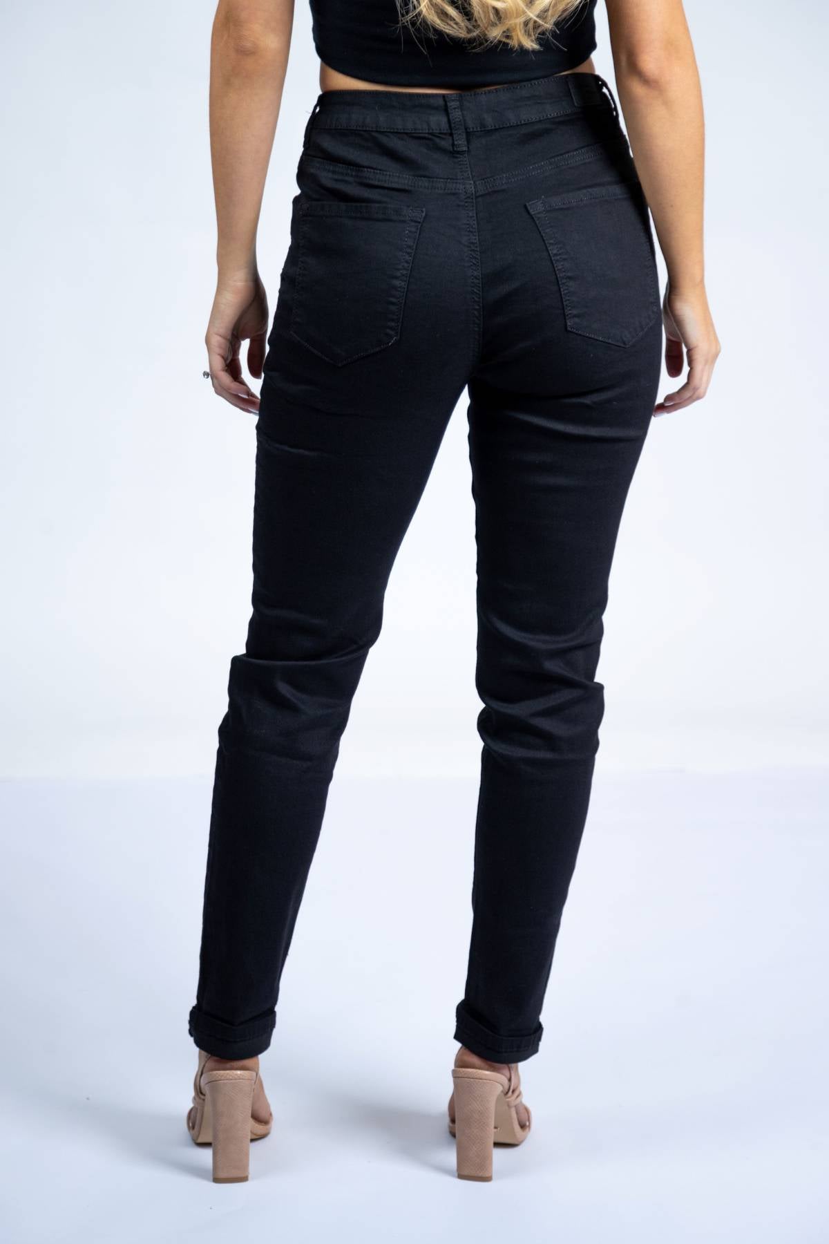 A woman faces away from the camera wearing Country Denim Relaxed Mum Jean in black, paired with a black crop top and nude heeled sandals, set against a plain white background.