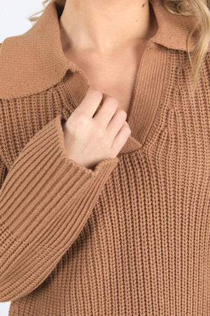 Close-up of a person wearing the Foxwood Carlton Knit, a relaxed fit light brown sweater with a wide collar. They're holding the collar with one hand, hair visible on the right, highlighting its comfort and stylish design.