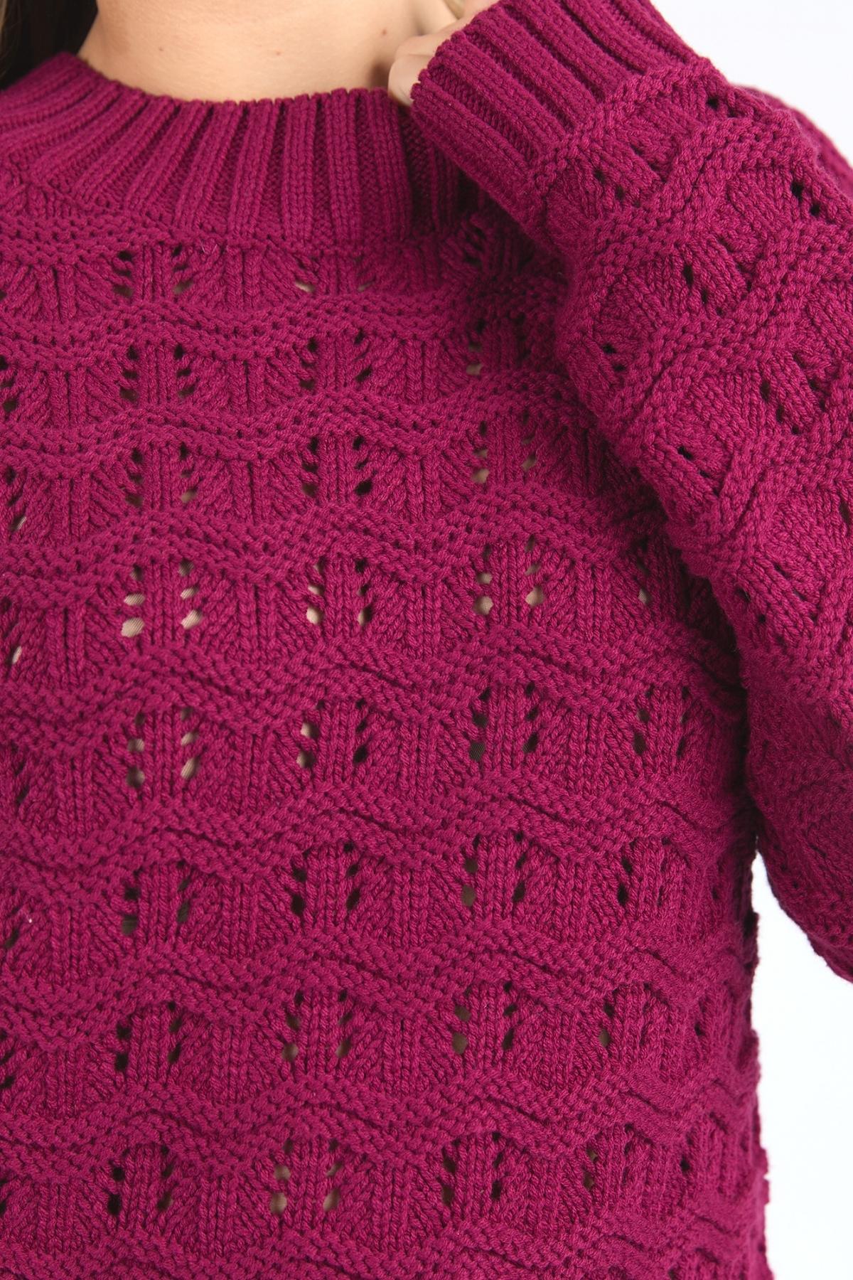 Close-up of someone wearing the Foxwood Carter Knit sweater in magenta, featuring a textured square pattern and ribbed cuffs and neckline. Made from a cotton acrylic blend for softness, with the wearer’s hand visible near the collar.