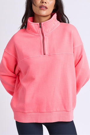 Wearing a loose-fitting, bright pink Foxwood College Zip Crew with the zipper partially open, the person stands against a plain light background. Only their upper body is visible.