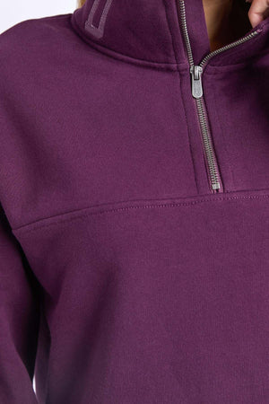 Close-up of a person wearing the Foxwood College Zip Crew—a purple 100% cotton zip-up pullover with a high collar, highlighting the textured fabric, embroidered collar, and zipper details.