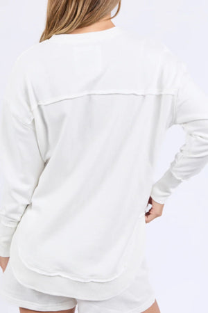A person with long, light brown hair is seen from behind wearing the Foxwood Simplified Confetti Crew, a loose white 100% cotton top with subtle multicoloured embroidery and matching shorts, against a plain light background.