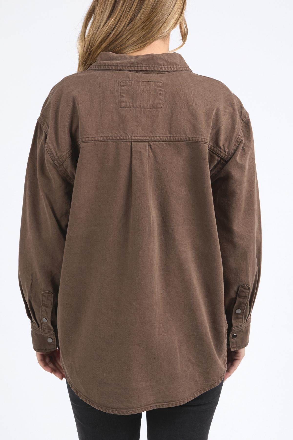 A person with long, light brown hair is seen from behind wearing the Foxwood Daisy Overshirt, a relaxed fit cotton shirt with a button-through placket and long sleeves, paired with black pants against a plain white background.