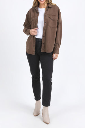 A person wears the Foxwood Daisy Overshirt in brown, styled over a white top with black jeans and beige ankle boots, standing against a plain white background. Their face is partially out of frame.