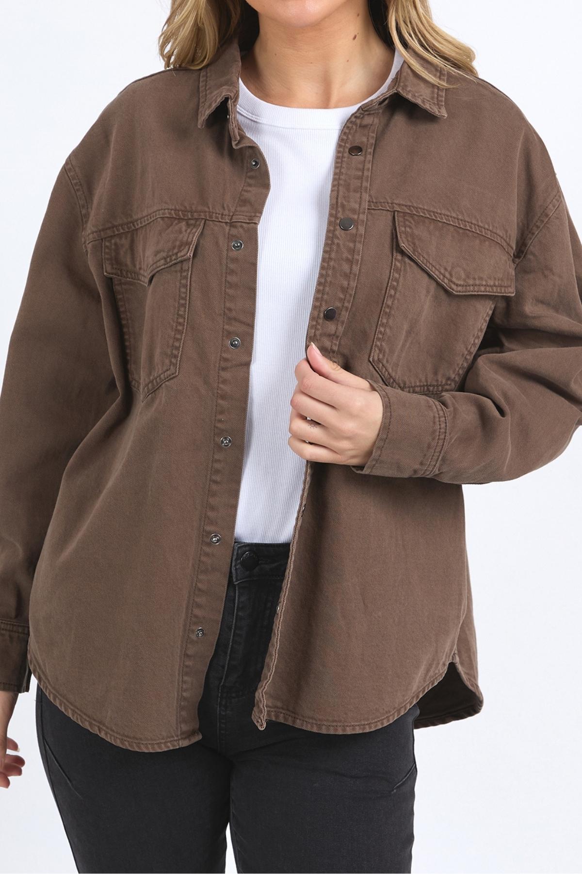 A person wears the Foxwood Daisy Overshirt—a relaxed fit brown cotton shirt with a button-through placket—over a white top and black pants, standing against a plain white background. Only the upper body is visible.