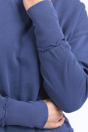 A person is shown from the shoulders down wearing the Foxwood Delilah Crew, crossing one arm over their body while the other arm is bent and partially covers their face.