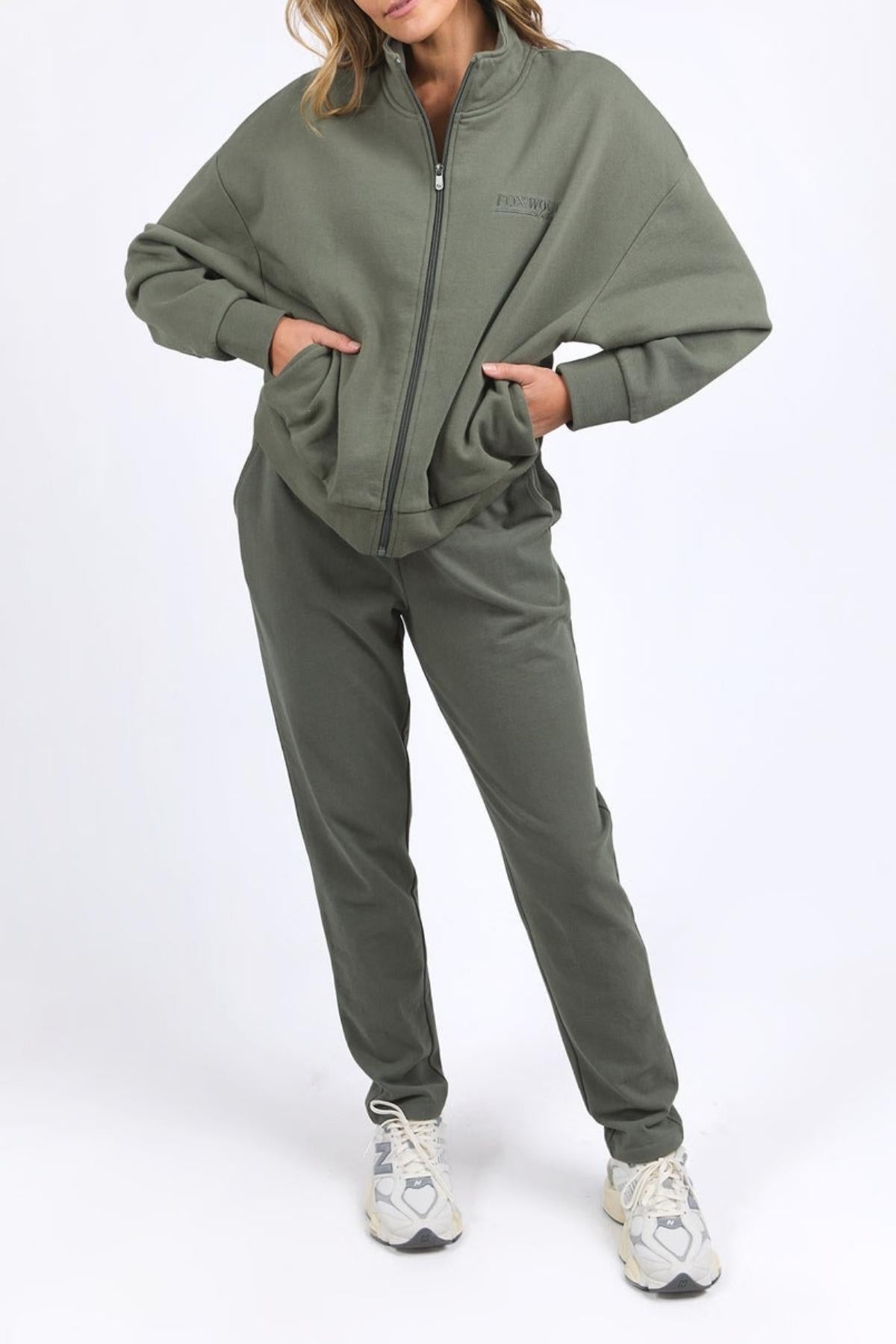 Wearing the Foxwood Ember Zip Thru jacket and matching joggers with a chest logo, hands in pockets, and white sneakers, a person stands against a plain white background.