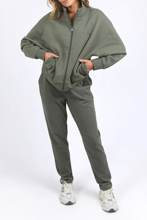Wearing the Foxwood Ember Zip Thru jacket and matching joggers with a chest logo, hands in pockets, and white sneakers, a person stands against a plain white background.