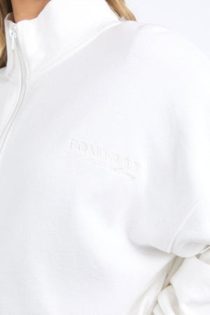 Close-up of someone wearing the Foxwood Ember Zip Thru brushed cotton fleece jacket, featuring an embroidered chest logo on a white sweatshirt, shown against a plain light background.