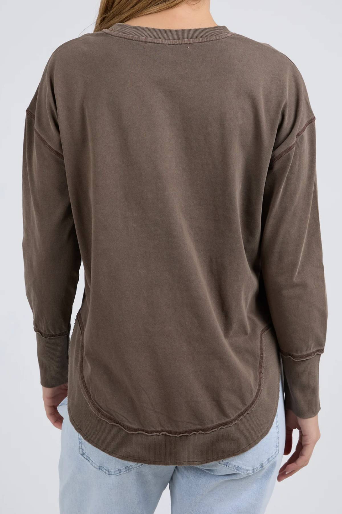 A person is shown from the back against a plain light background, wearing the relaxed fit Foxwood Farrah Long Sleeve in brown and light blue jeans.