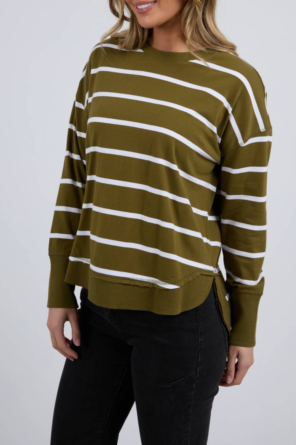 A woman wears the Foxwood Farrah Stripe Long Sleeve in olive green with white stripes, made from 100% Fresh Pima Cotton, paired with black jeans against a plain light background.