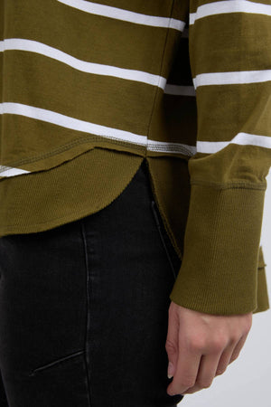 Close-up of a person wearing the Foxwood Farrah Stripe Long Sleeve in green and white, made from 100% Fresh Pima Cotton. The rounded, ribbed hem and cuffs pair with black pants, as their hand rests naturally by their side.