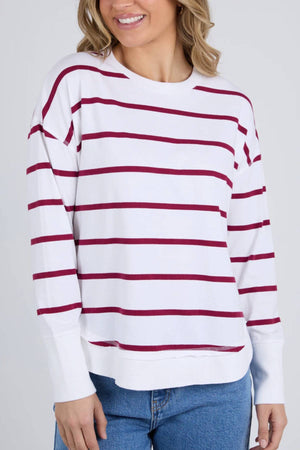 A woman smiles against a plain light background wearing the Foxwood Farrah Stripe Long Sleeve, featuring white fabric with horizontal maroon stripes and paired with blue jeans.