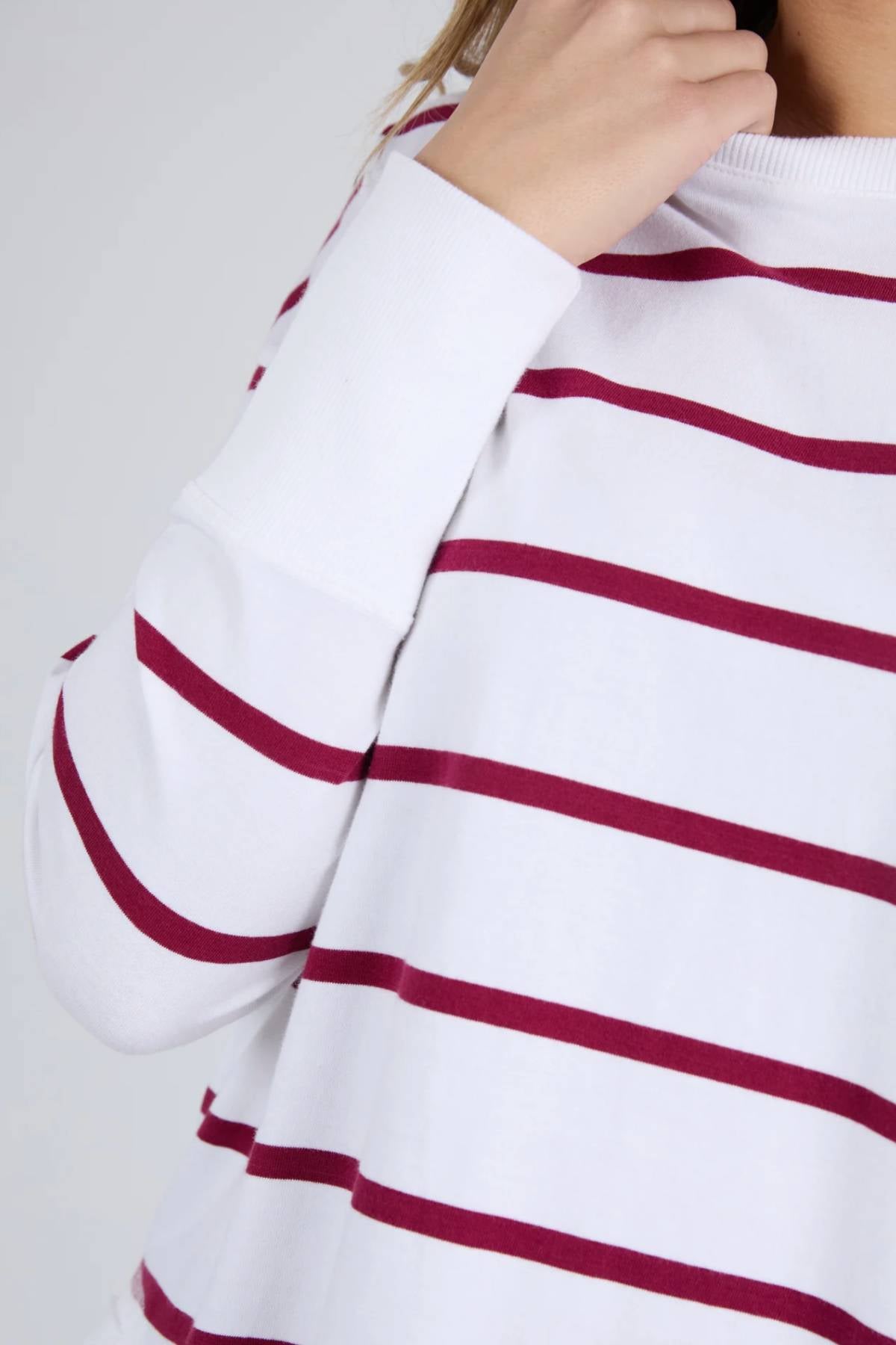 A person is shown from the shoulders down, wearing the Foxwood Farrah Stripe Long Sleeve in soft Pima Cotton with maroon stripes on a white base, one hand touching their neck against a plain light background.