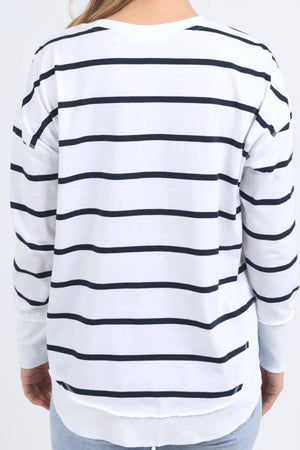 A person is seen from the back wearing a Foxwood Farrah Stripe Long Sleeve in white with black horizontal stripes. The relaxed fit jumper is loose and paired with light blue jeans.