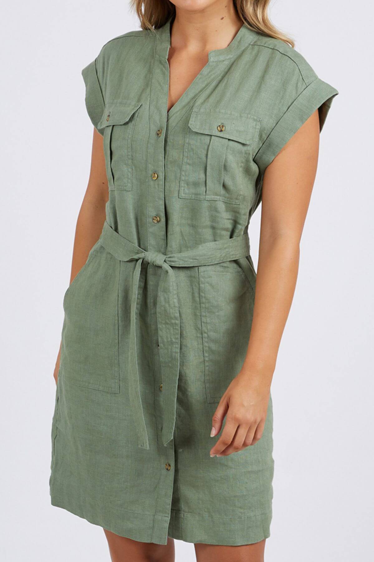 A woman models the Foxwood Harlow Dress—short-sleeved, sage green, with a belted waist and two chest pockets—standing against a plain light background for a smart-casual summer look.