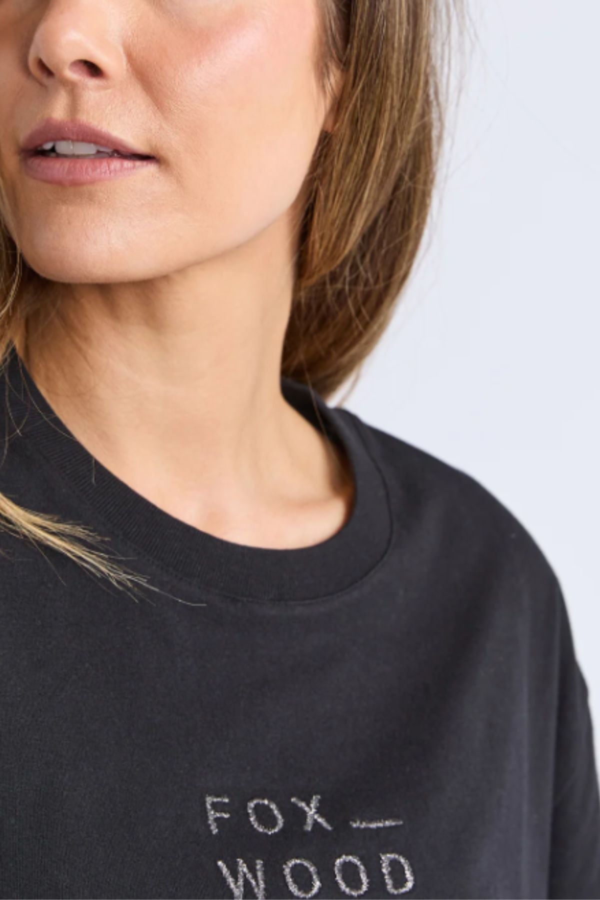 A woman models the Foxwood Huntleigh Oversized Tee in premium cotton, showing only her lower face and upper torso with partially visible "FOX WOOD" text on the shirt.