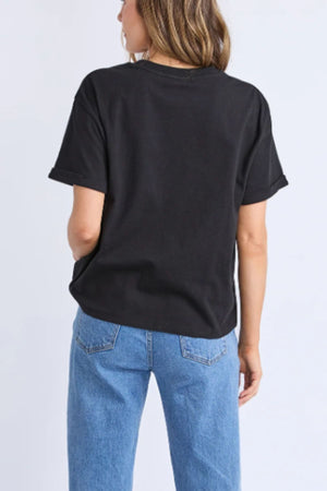 A person with light brown hair faces away, wearing the Foxwood Huntleigh Oversized Tee in black with blue jeans, set against a plain light background.