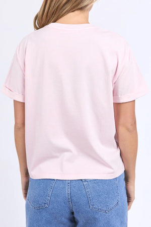 A person with light brown hair is seen from the back wearing the Foxwood Huntleigh Oversized Tee in light pink cotton, paired with high-waisted blue jeans against a plain light background.