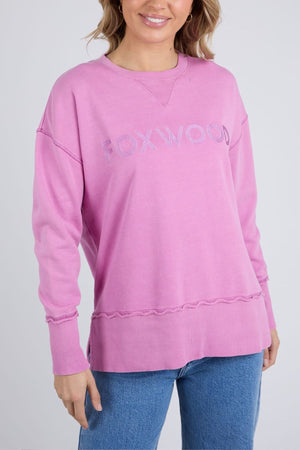 A woman wears the Foxwood Illusion Crew, a relaxed fit sweatshirt in soft cotton fleece with an embroidered logo on the chest, paired with blue jeans against a plain light background.