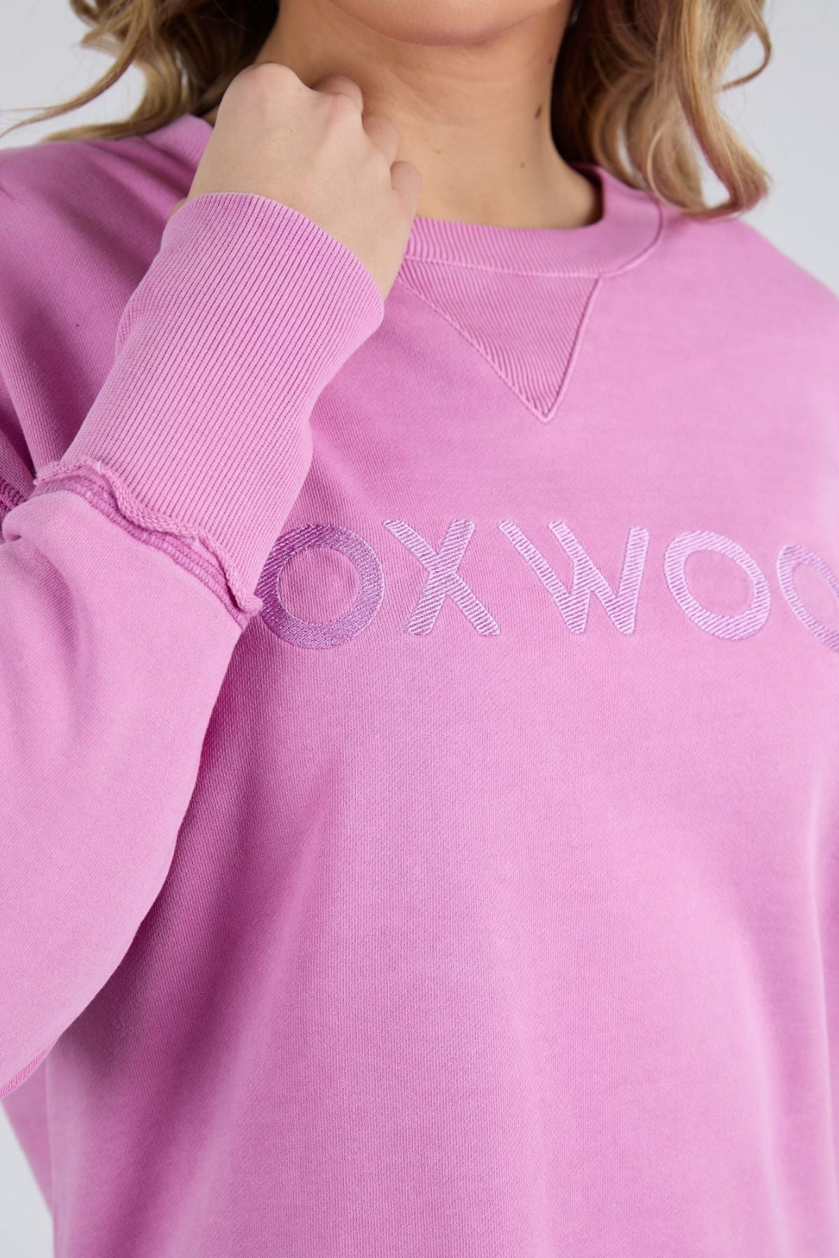 Someone wearing the Foxwood Illusion Crew, a light purple relaxed-fit sweatshirt made from soft cotton fleece, featuring a partially visible embroidered "OXWOO" on the front and shown from shoulders to mid-torso.