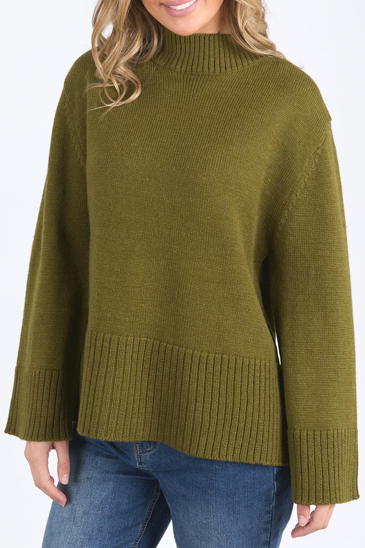 A woman models the Foxwood Jude Knit, a relaxed fit olive green sweater with a mock neck, paired with blue jeans. Only her torso and lower face are shown against a plain background.