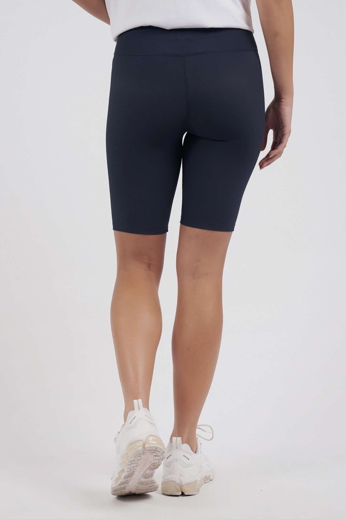 A person is shown from the back against a plain light background, wearing a white shirt, white sneakers, and navy blue Foxwood Luxe Rib Shorts with an elastic waist.
