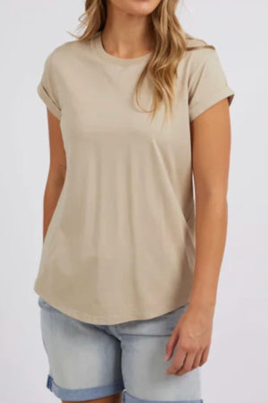 A woman wears the Foxwood Manly Tee, made from soft 100% cotton with rolled cuffs, paired with light denim shorts. Against a plain backdrop, her partially out-of-frame face adds to the effortless, casual chic style.