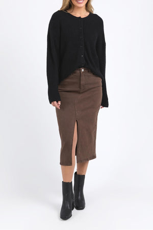 A woman wears the Foxwood Murphy Knit Cardi in black, styled with a brown knee-length skirt featuring a front slit and black ankle boots, standing against a plain white background.