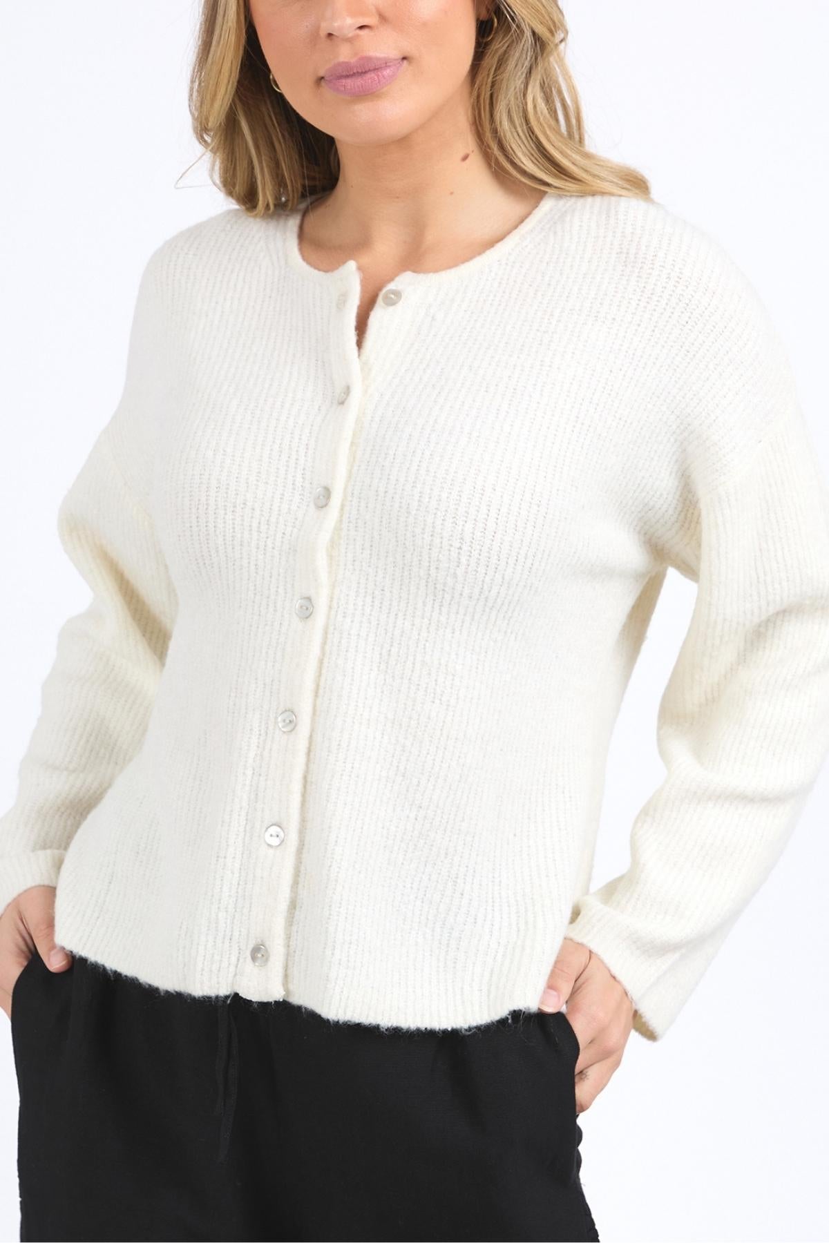 A woman wears the Foxwood Murphy Knit Cardi—a cozy, stylish white knit with a relaxed fit and ribbed texture—paired with black pants, standing against a plain white background.