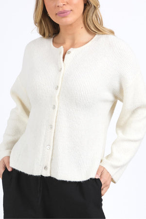 A woman wears the Foxwood Murphy Knit Cardi—a cozy, stylish white knit with a relaxed fit and ribbed texture—paired with black pants, standing against a plain white background.