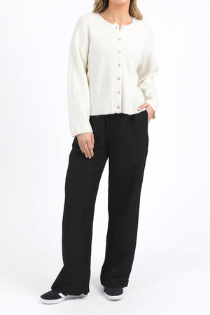 A person stands against a white background, wearing the cozy and stylish Foxwood Murphy Knit Cardi with a relaxed fit, paired with black wide-leg pants and sneakers. One hand is in their pocket, head slightly turned to the side.